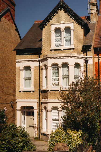A close-up view of a front garden entrance in Penge, featuring a deep red wooden door with a brass letterbox and decorative latch, set within a white painted frame with classic architectural detailing